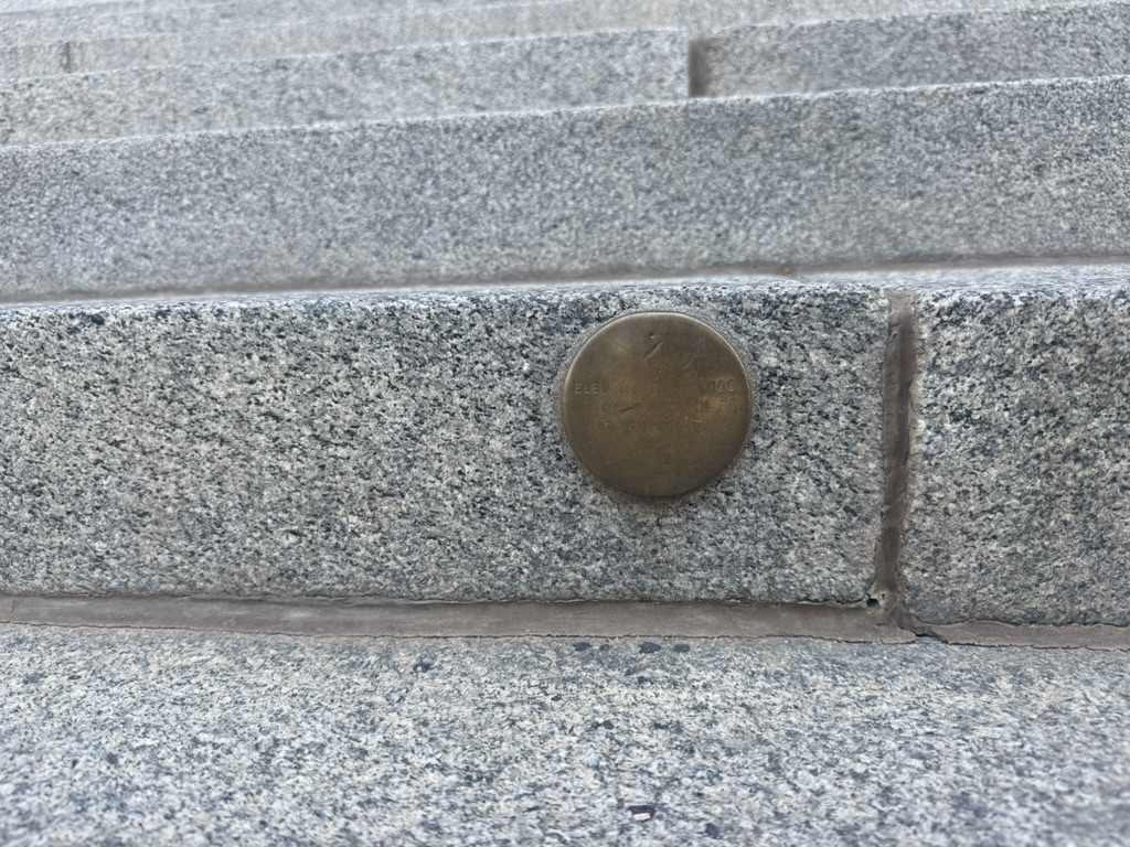 Close-up of a worn brass survey marker set flush into a granite step
