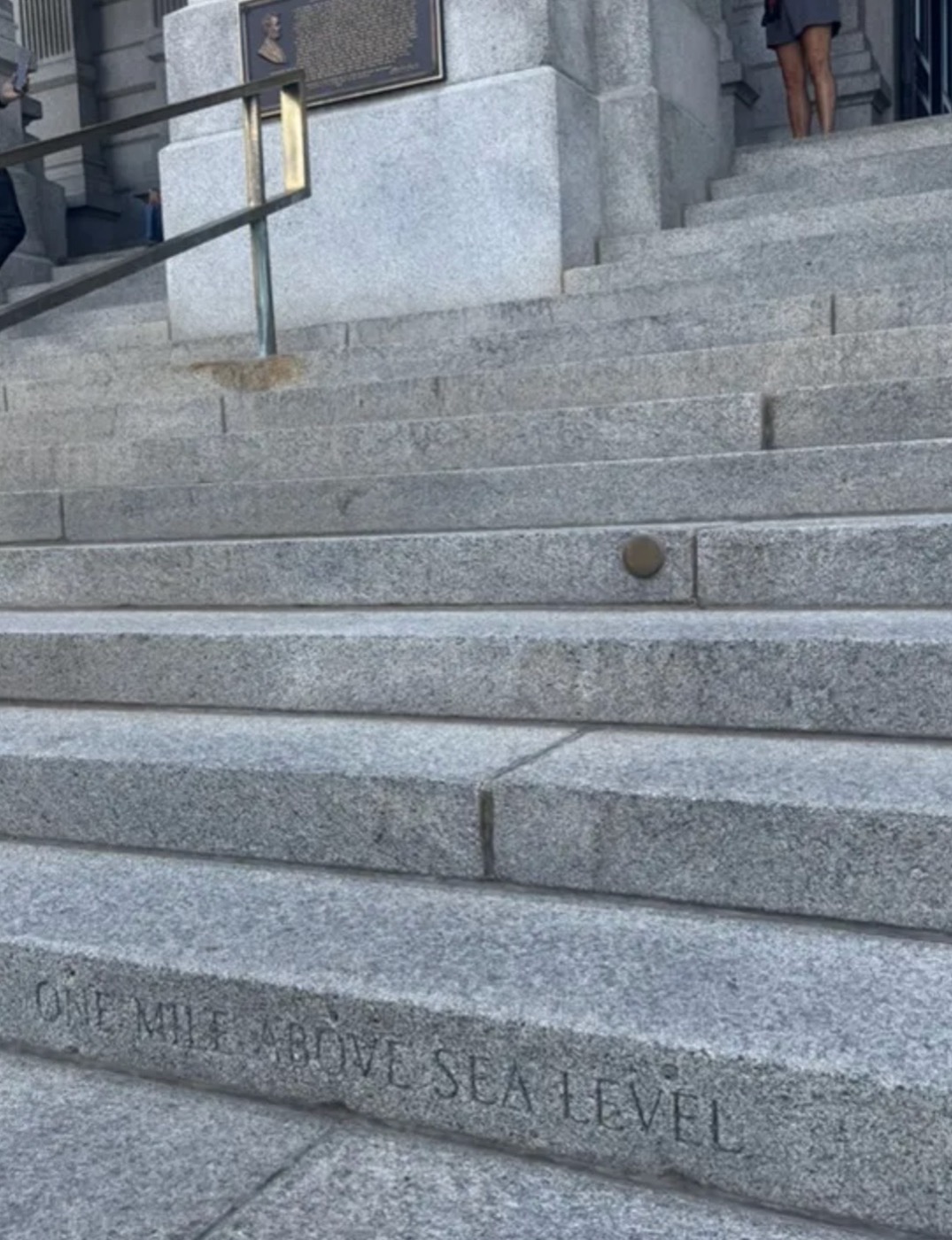 Granite steps of the Colorado State Capitol: ONE MILE ABOVE SEA LEVEL carved into the lower step, with a small brass survey marker set into a step three above it